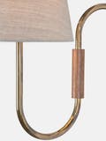 A curved wall light made from brass tubing and walnut accents with a thumb-turn switch and linen shade.