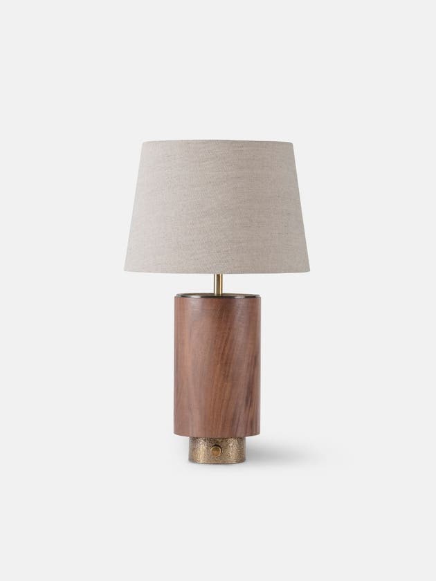 Table light with a walnut body, textured brass base, thumb turn switch, and linen shade - Light off.