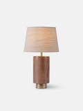 Table light with a walnut body, textured brass base, thumb turn switch, and linen shade - Light on.