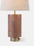 Table light with a walnut body, textured brass base, thumb turn switch, and linen shade.