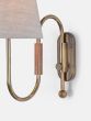 A curved wall light made from brass tubing and walnut accents with a thumb-turn switch and linen shade.